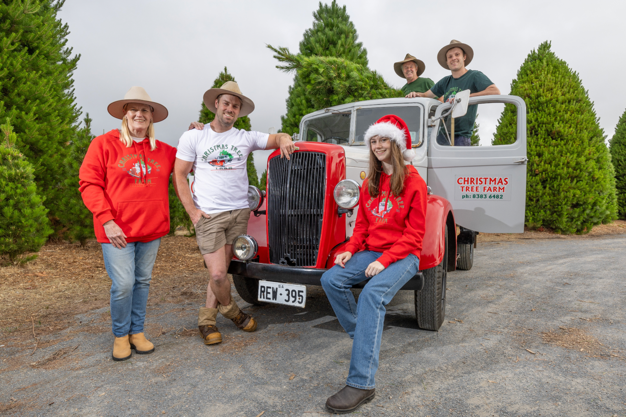 Photo of the family who run Chandlers Hill Christmas Tree Farm standing with the farm’s delivery truck in front of the forest filled with fresh Christmas trees, showcasing the family-run Christmas Tree Farm, festive holiday atmosphere, and lush forest scenery