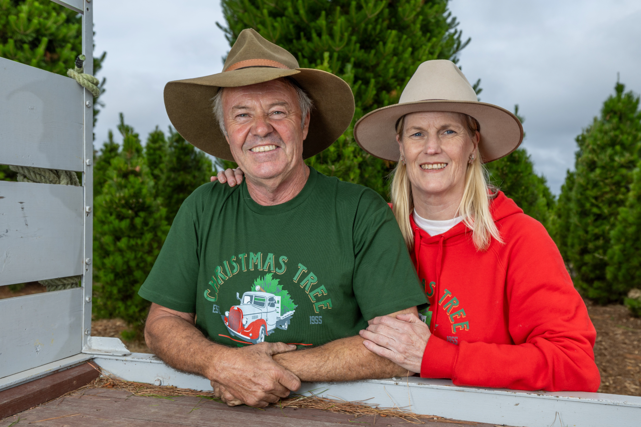 Photo of the two owners of Chandlers Hill Christmas Tree Farm standing with the farm’s delivery truck in front of the forest filled with fresh Christmas trees, showcasing the family-run farm, festive holiday atmosphere, and lush forest scenery
